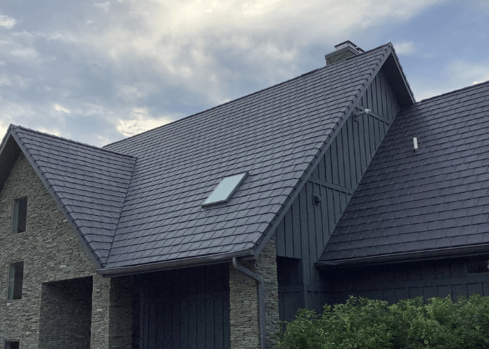 Close-up view of a gray slate roof with multiple steep gables on a stone-covered building under a cloudy sky.