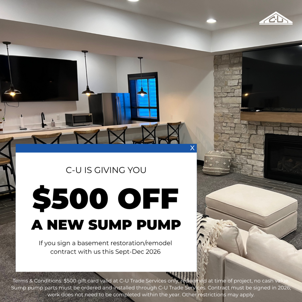 Finished basement with a stone fireplace, wall-mounted TVs, a kitchenette, and seating area. Overlay text reads: C-U is giving you $500 off a new sump pump if you sign a basement restoration or remodel contract with us this September through December 2026.